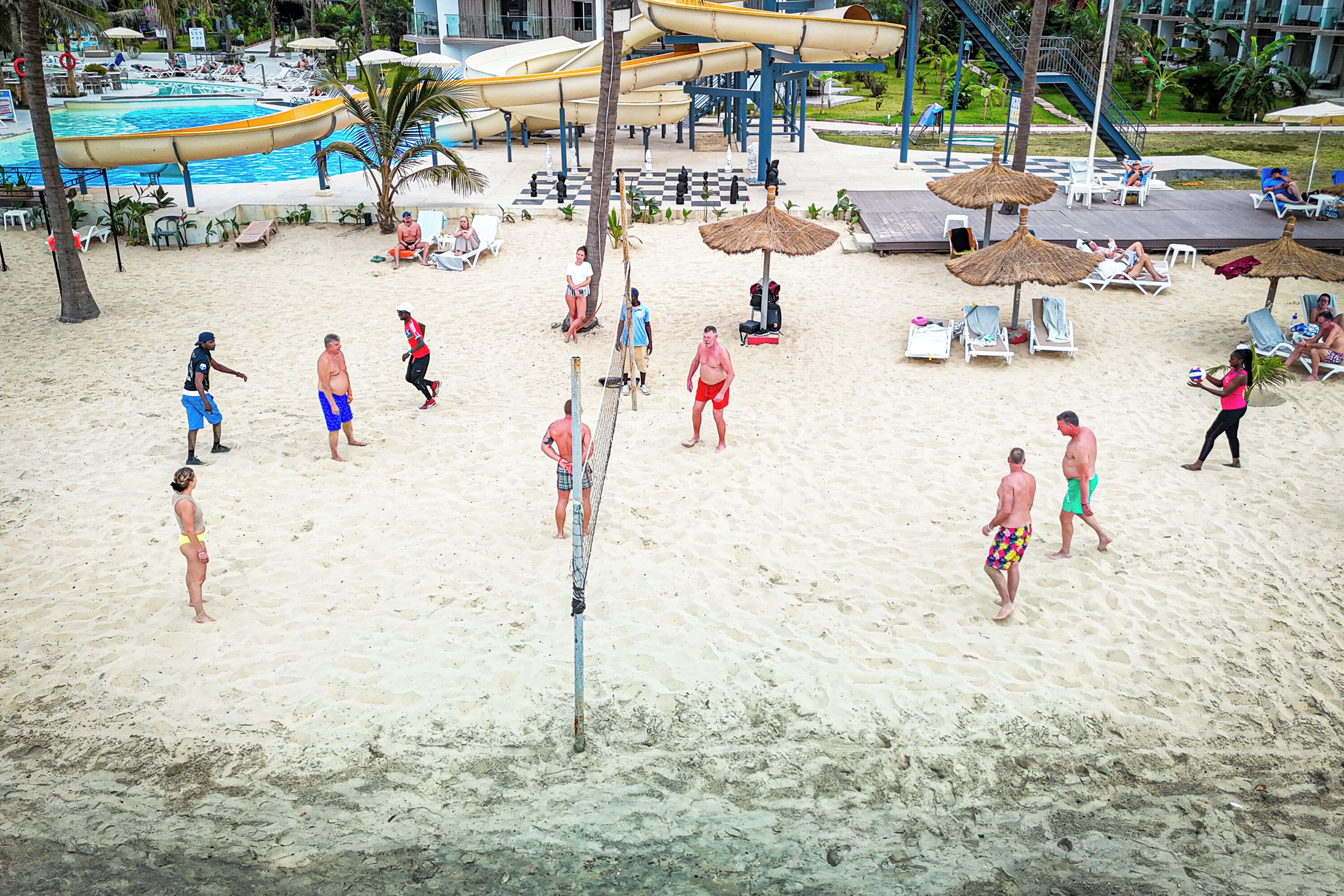 A beach volleyball court with people playing, surrounded by lounge chairs and umbrellas.