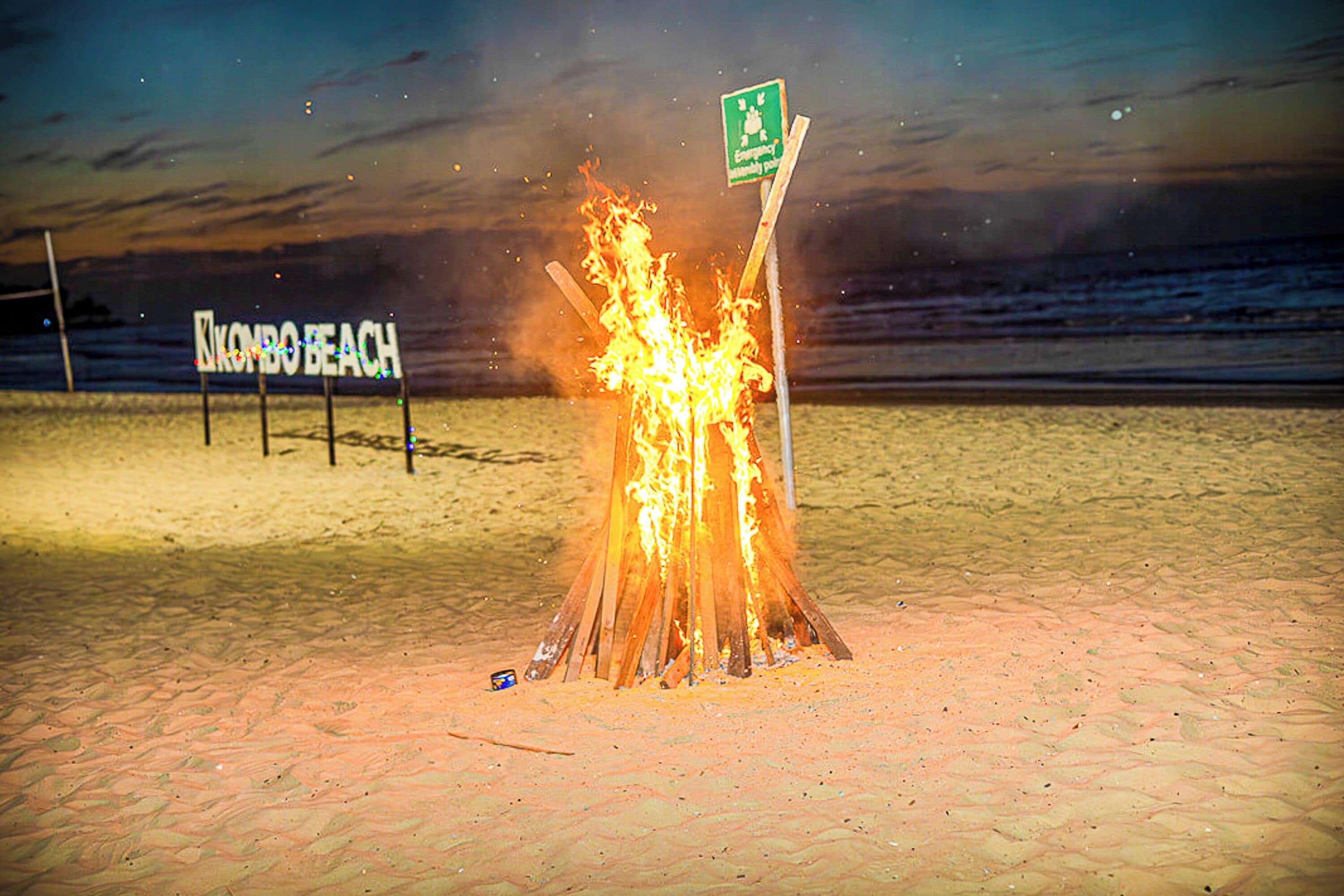Escena de playa con una fogata y un letrero que dice "KONBO BEACH".