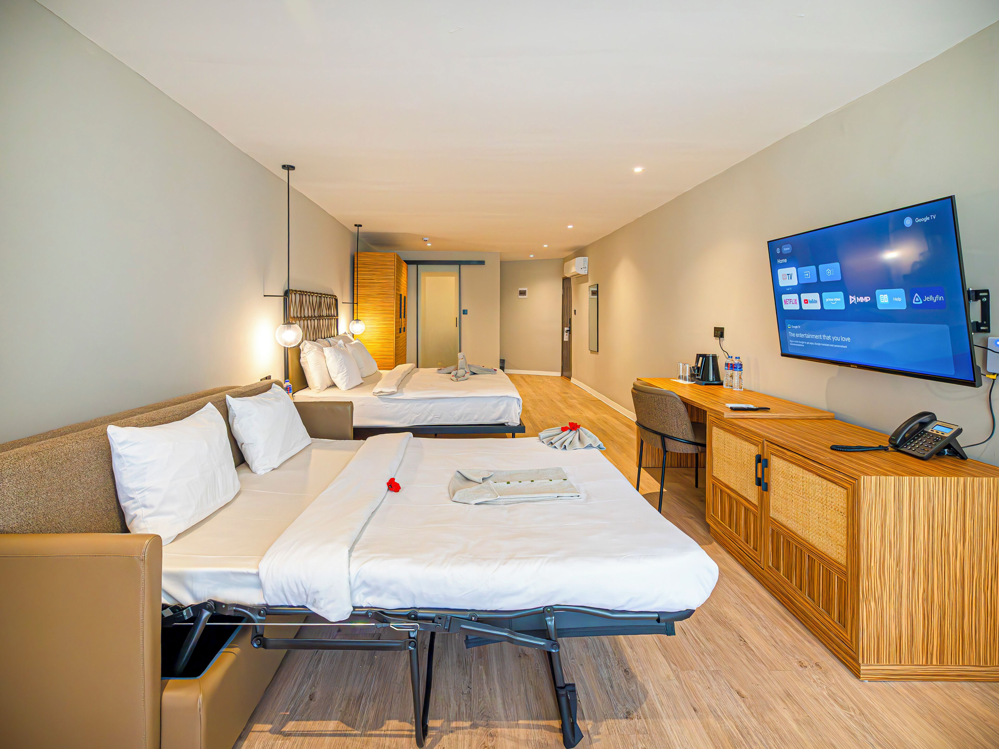 A hotel room with two beds, a desk, a TV, and a wooden cabinet.
