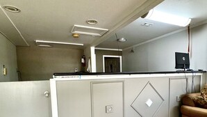 A hotel reception area with a grey reception desk, a black HP monitor, a red carpet with "Best Budget Inn" text, and a tiled floor. - Best Budget Inn - Abilene (Abilene)