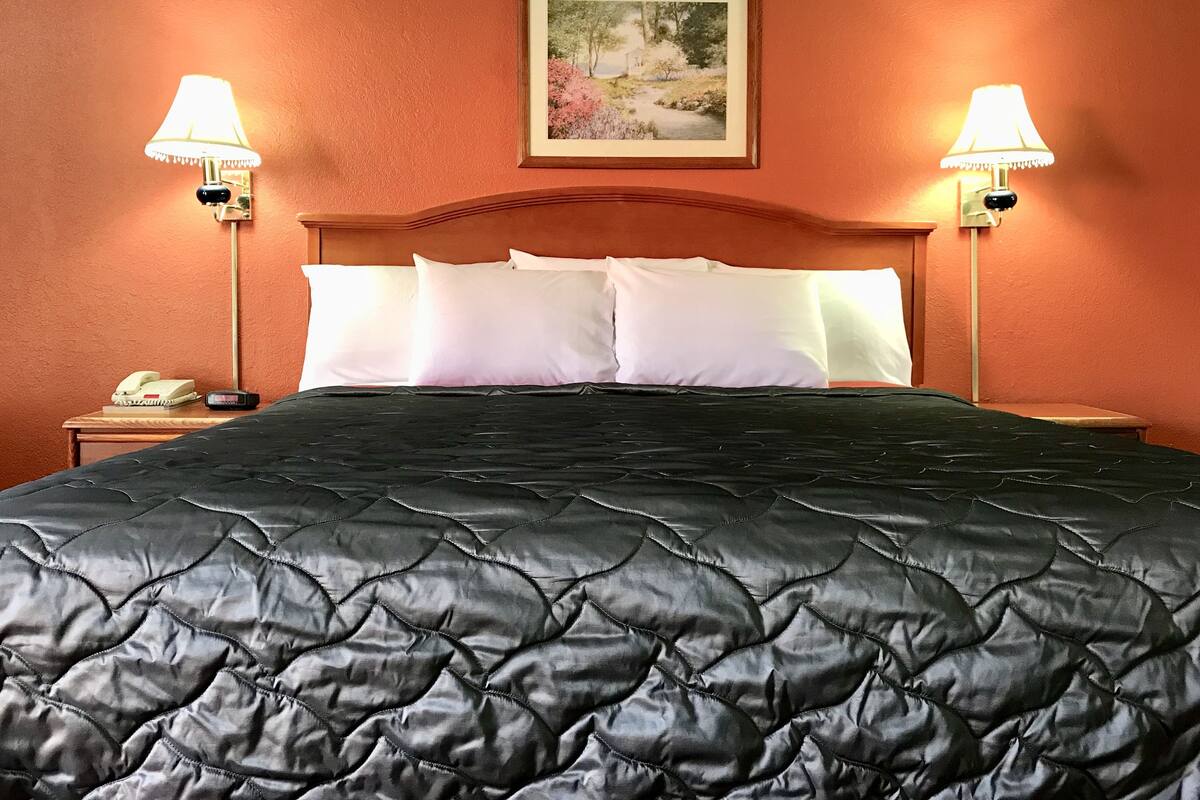 A hotel room with a bed, two bedside lamps, a framed picture on the wall, and a telephone on the nightstand.