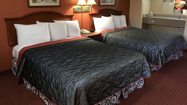 A hotel room with two beds, a nightstand, a telephone, two wall-mounted lamps, a mirror, and two framed pictures on the wall. - Best Budget Inn - Abilene (Abilene)