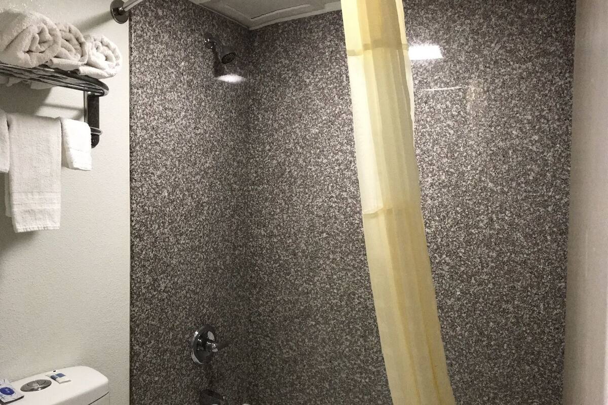 A bathroom with a white bathtub, a shower curtain, a toilet, and a towel rack with towels.