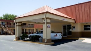 A motel with a covered parking area, a white car parked inside, and a staircase leading to an upper level. - Best Budget Inn - Abilene (Abilene)