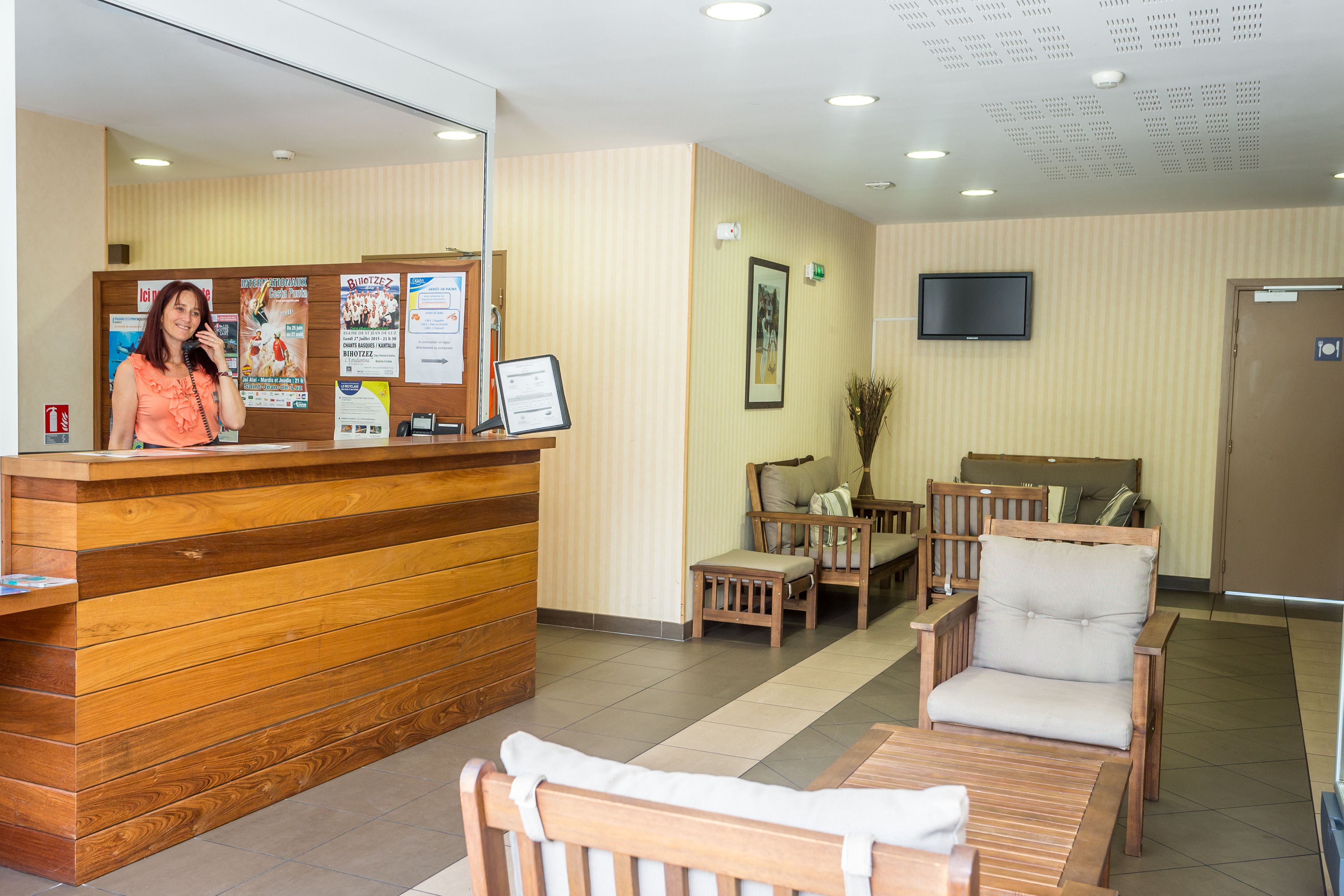 A reception area with a wooden reception desk, a seated receptionist, and a seating area with wooden furniture.