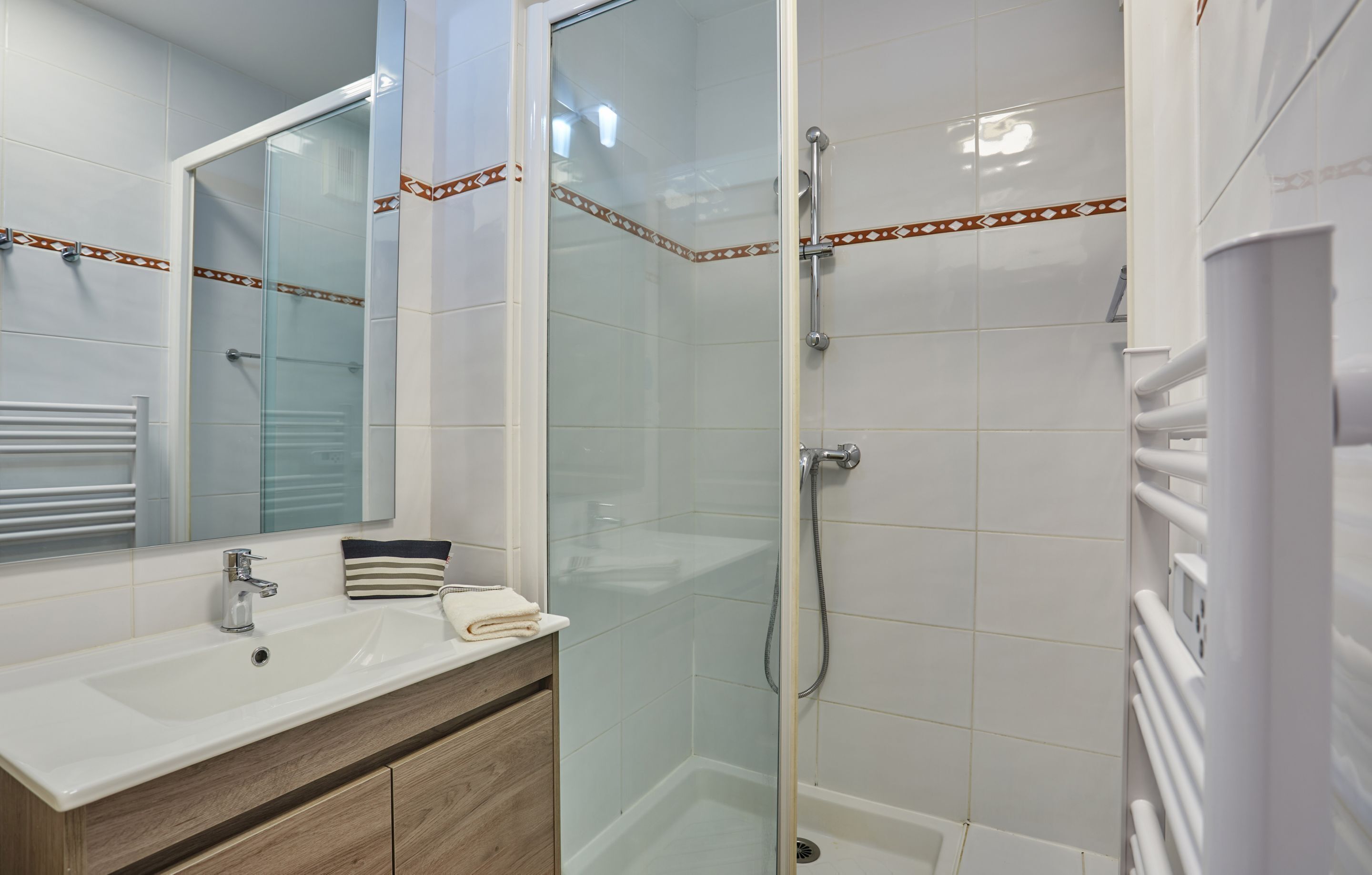 Un baño moderno con ducha envuelta en vidrio, lavamanos blanco y tocador de madera.