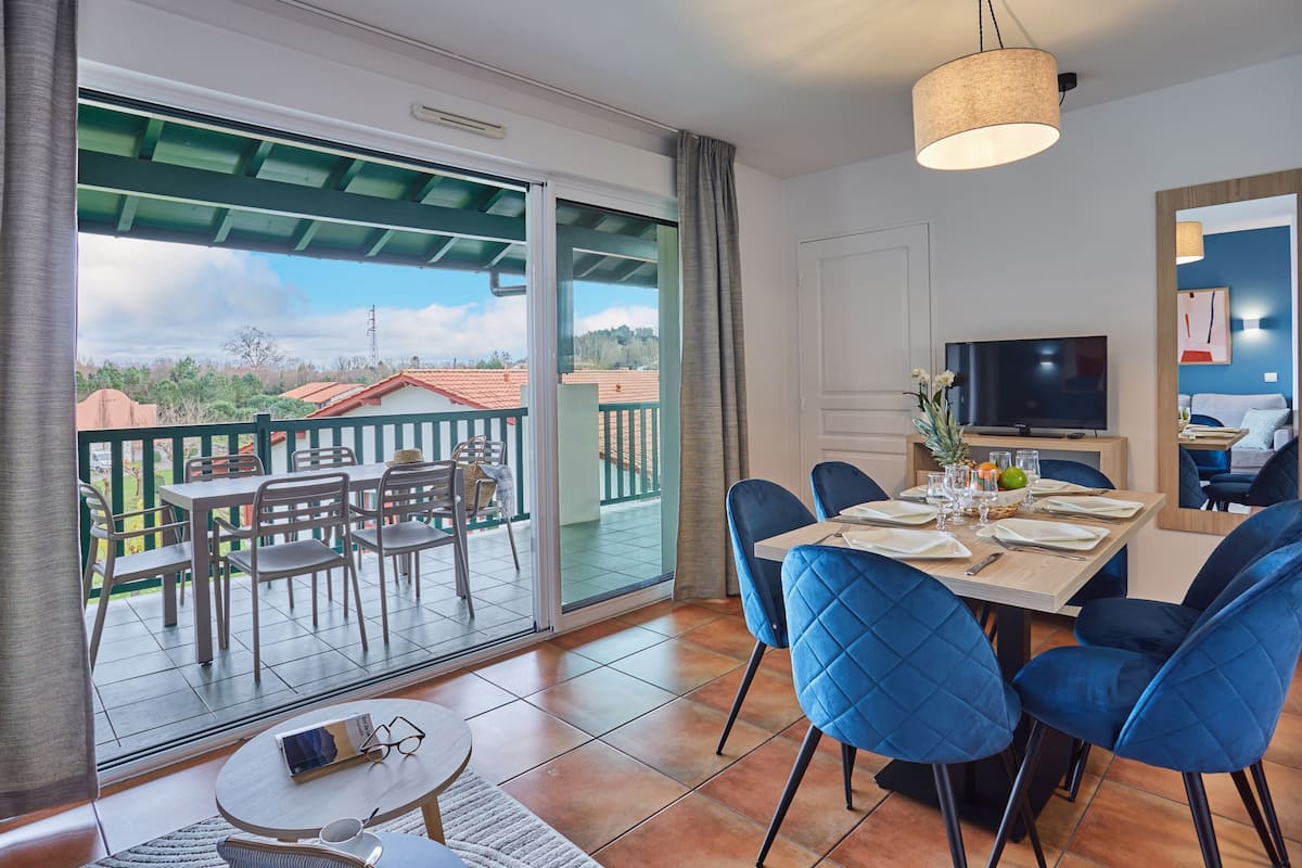 Ein Essbereich mit Tisch für zwei Personen, einem Fernseher und einem Balkon mit Sitzgelegenheit.