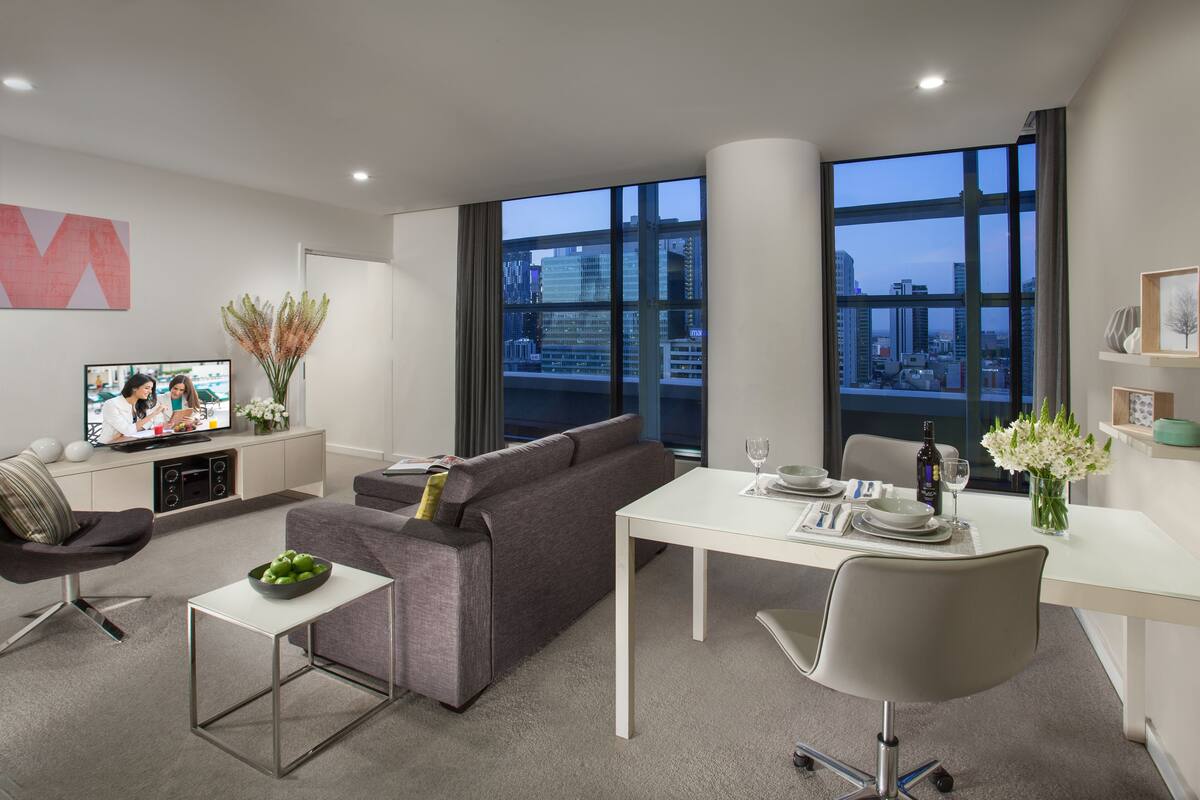 A modern living room with a grey sofa, a white dining table, and a TV on a cabinet.