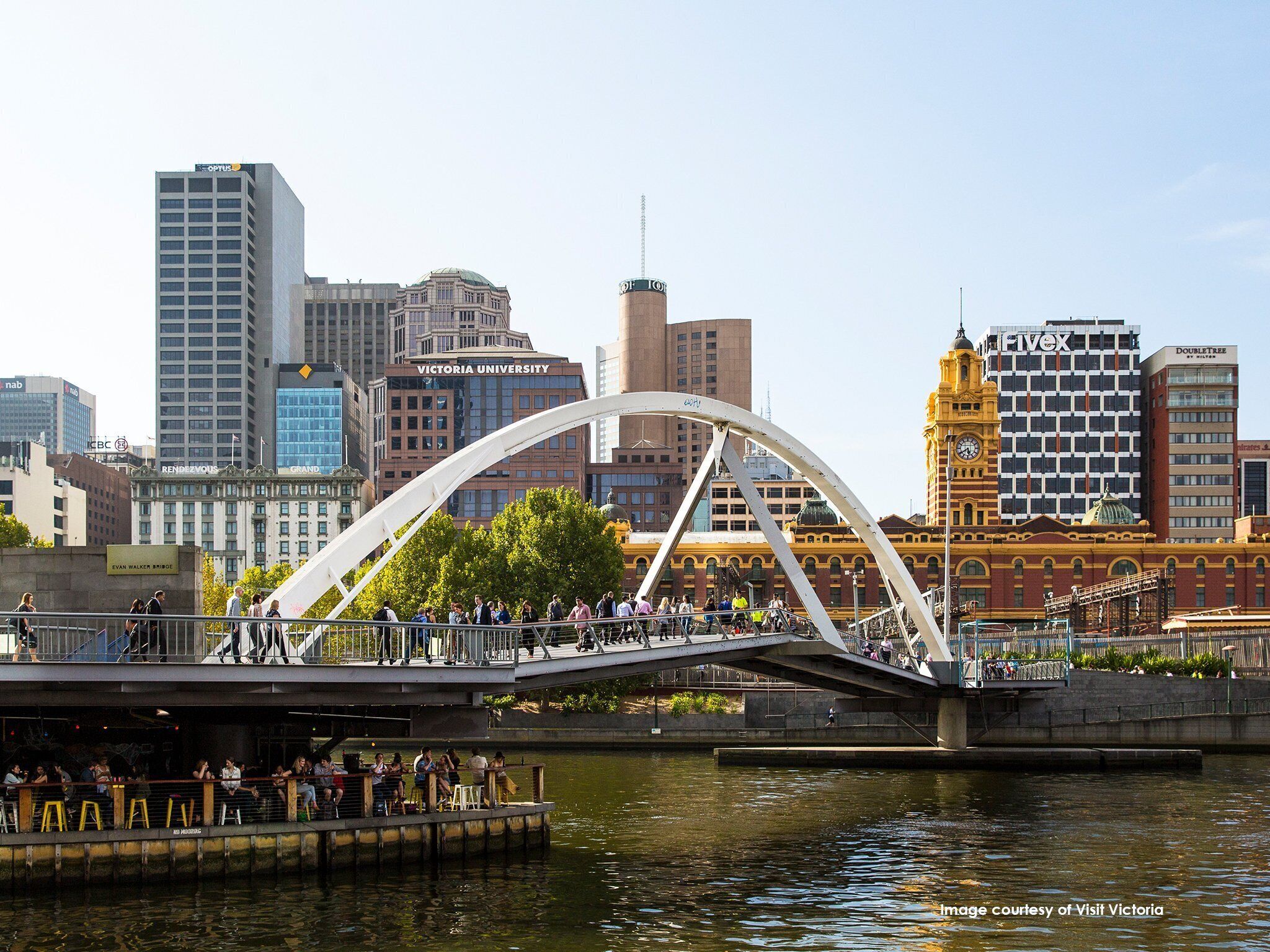 A bridge with a white arch structure over a body of water, with people walking on it.