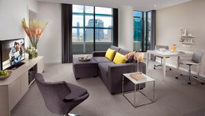 Uma sala de estar moderna com um sofá cinzento, uma mesa de centro, uma televisão e um espaço de jantar com uma mesa e cadeiras brancas.