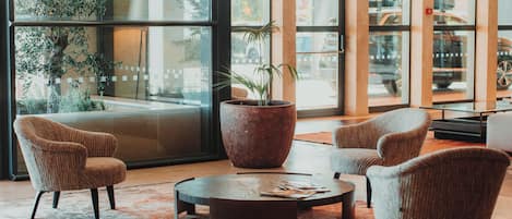 A lobby with a large potted plant, a round coffee table, and four armchairs.