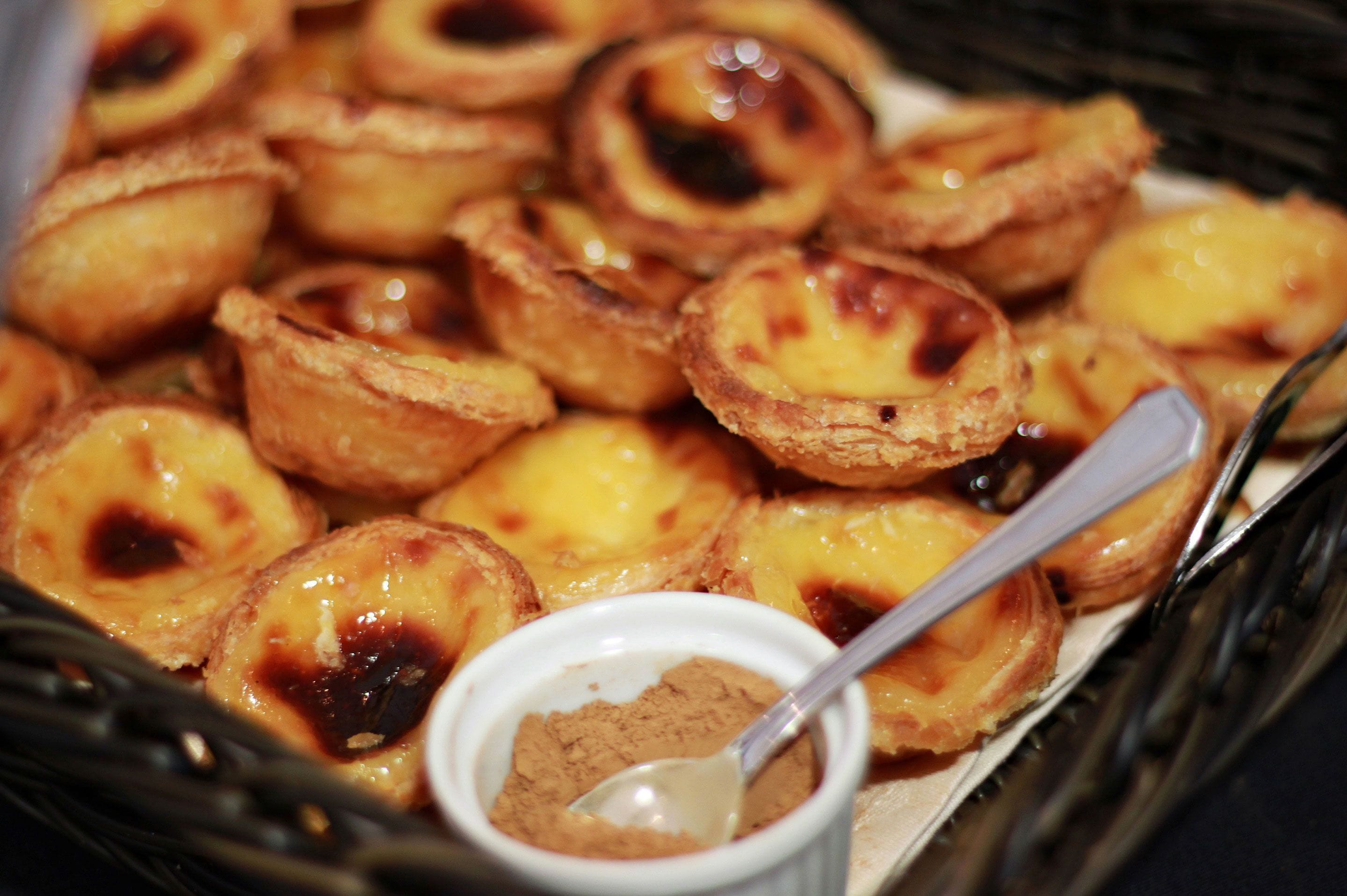 Uma bandeja de pastéis de nata portugueses, com uma colher e uma pequena tigela de açúcar em pó.