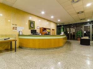 A reception area with a curved counter, a computer, a framed picture, and a bulletin board. - Covadonga Apartamentos Turisticos (Bormujos)