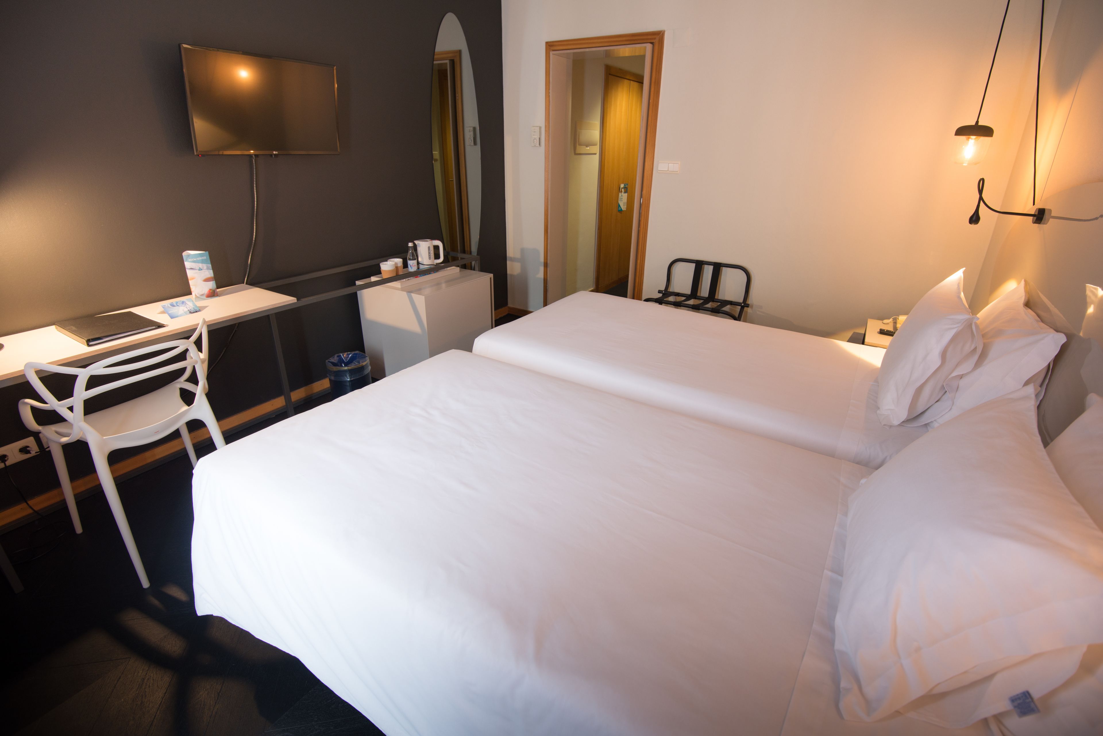 A hotel room with a bed, a desk, a chair, a TV, and a mirror.
