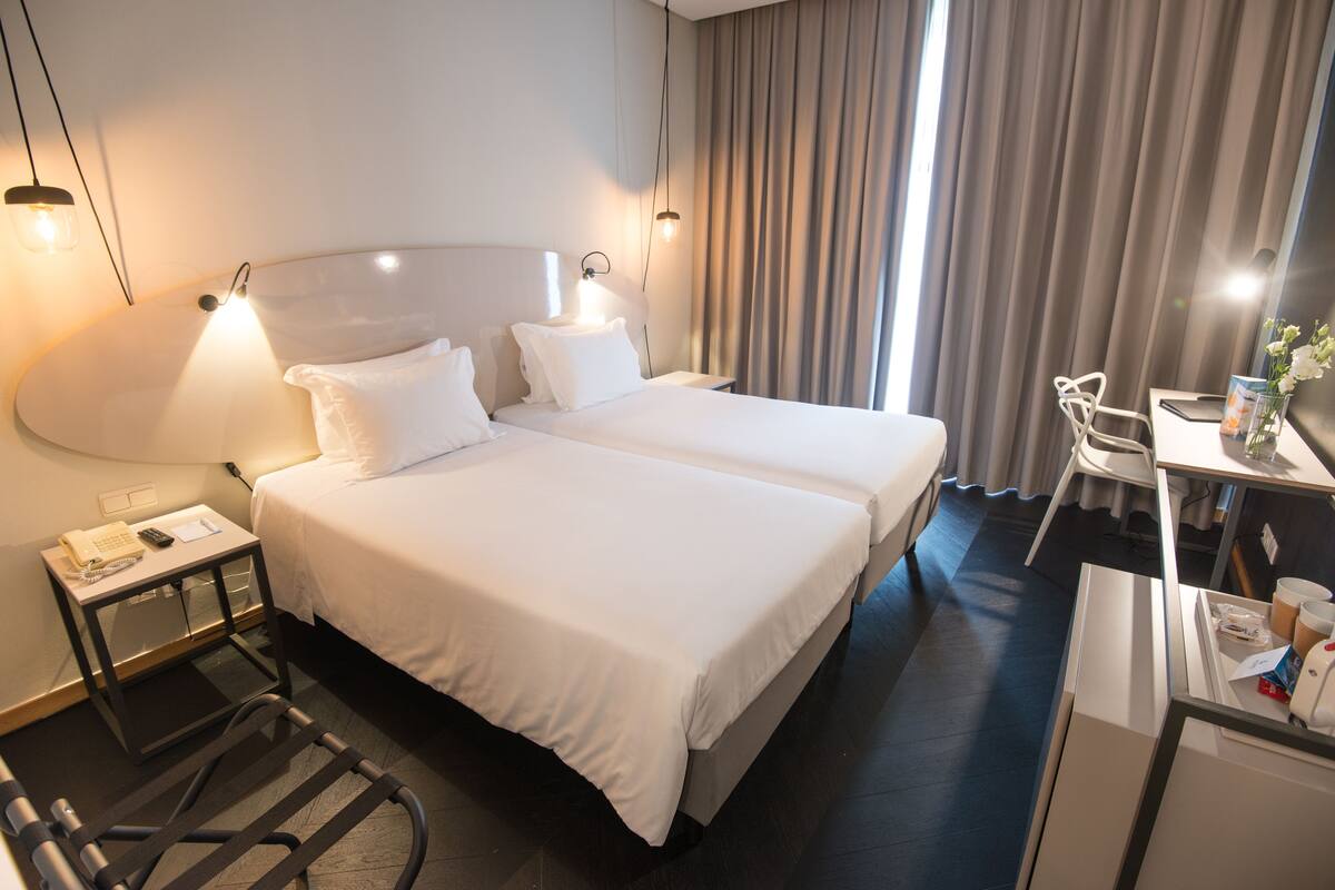 A hotel room with two beds, a desk, a chair, and a small table with a vase of flowers.