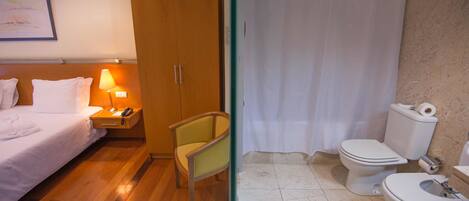 A hotel room with a bed, nightstand, lamp, chair, and a bathroom with a toilet and shower curtain.