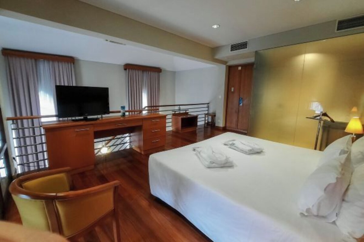A hotel room with a bed, desk, chair, television, and a lamp.
