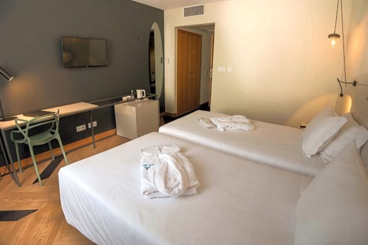 A hotel room with two beds, a desk, a chair, and a television on the wall.
