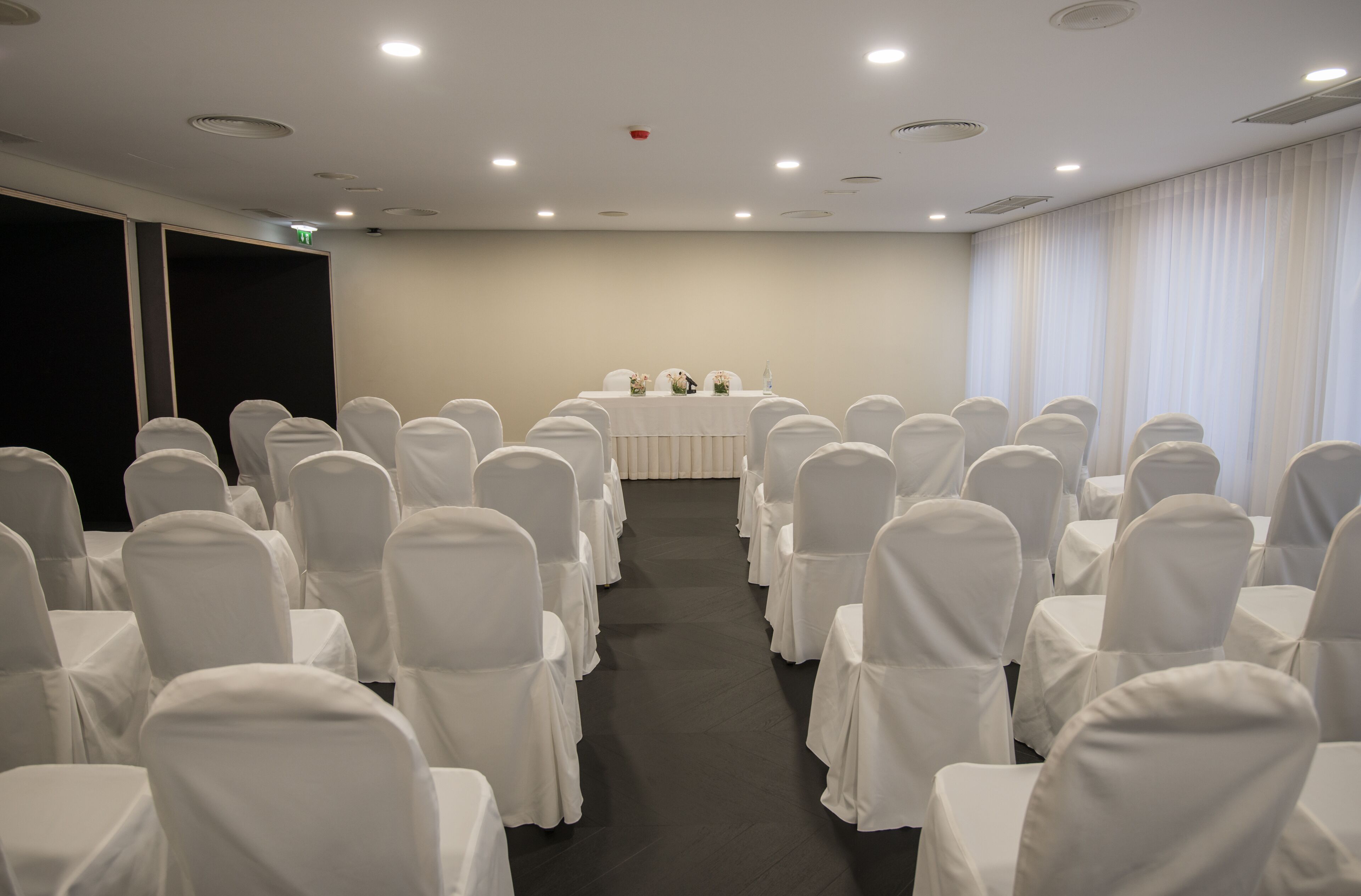 Ein Konferenzraum mit Reihen weiß bezogener Stühle und einem Tisch an der Vorderseite.