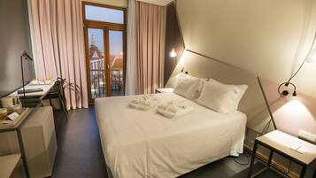 A hotel room with a bed, a desk, a chair, and a view of a building through the window.