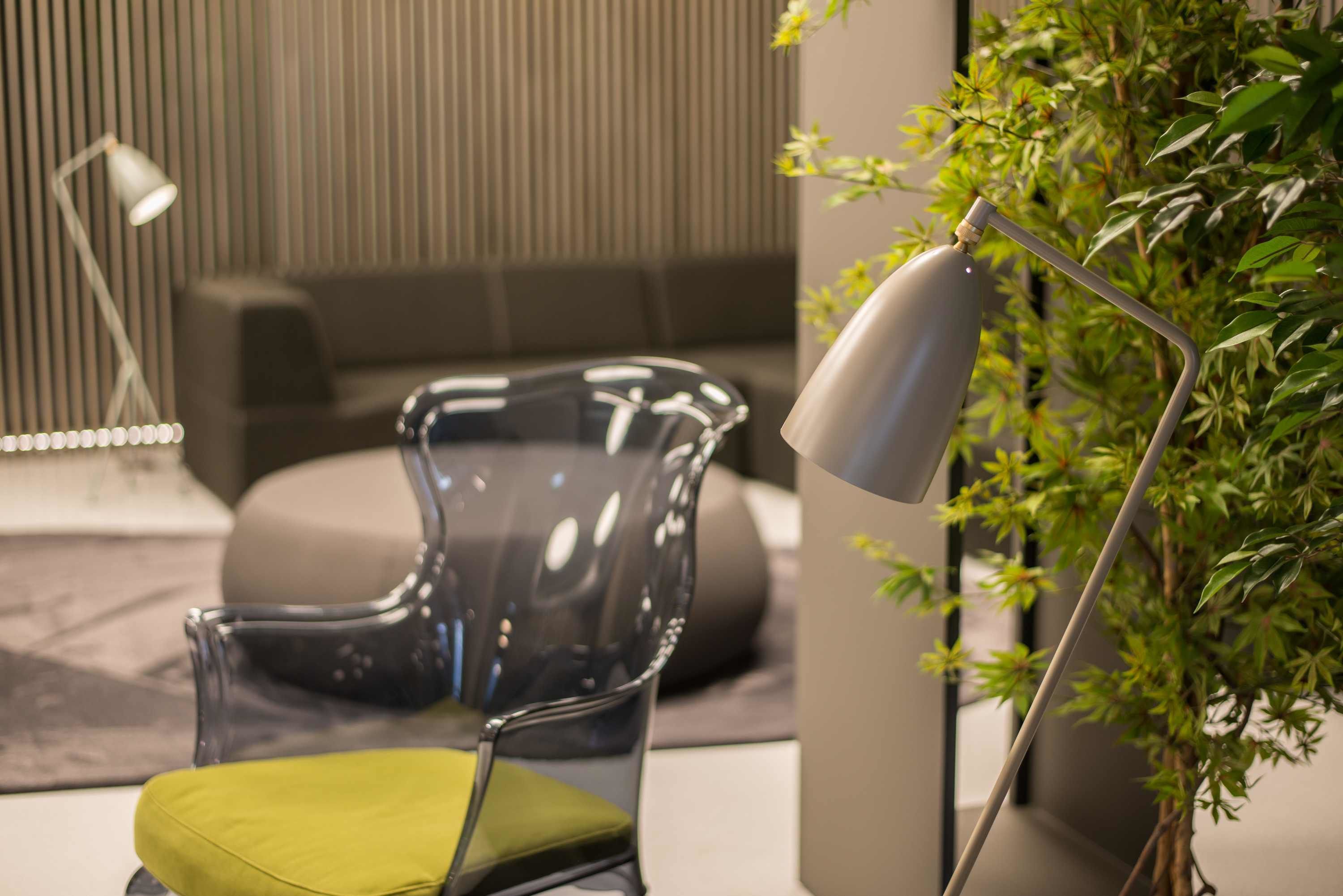 A modern room with a clear glass chair, a floor lamp, and a potted plant.