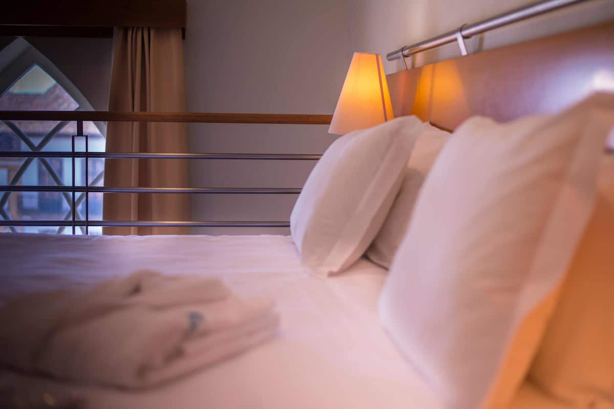 A hotel room with a bed, a nightstand with a lamp, and a window with curtains.