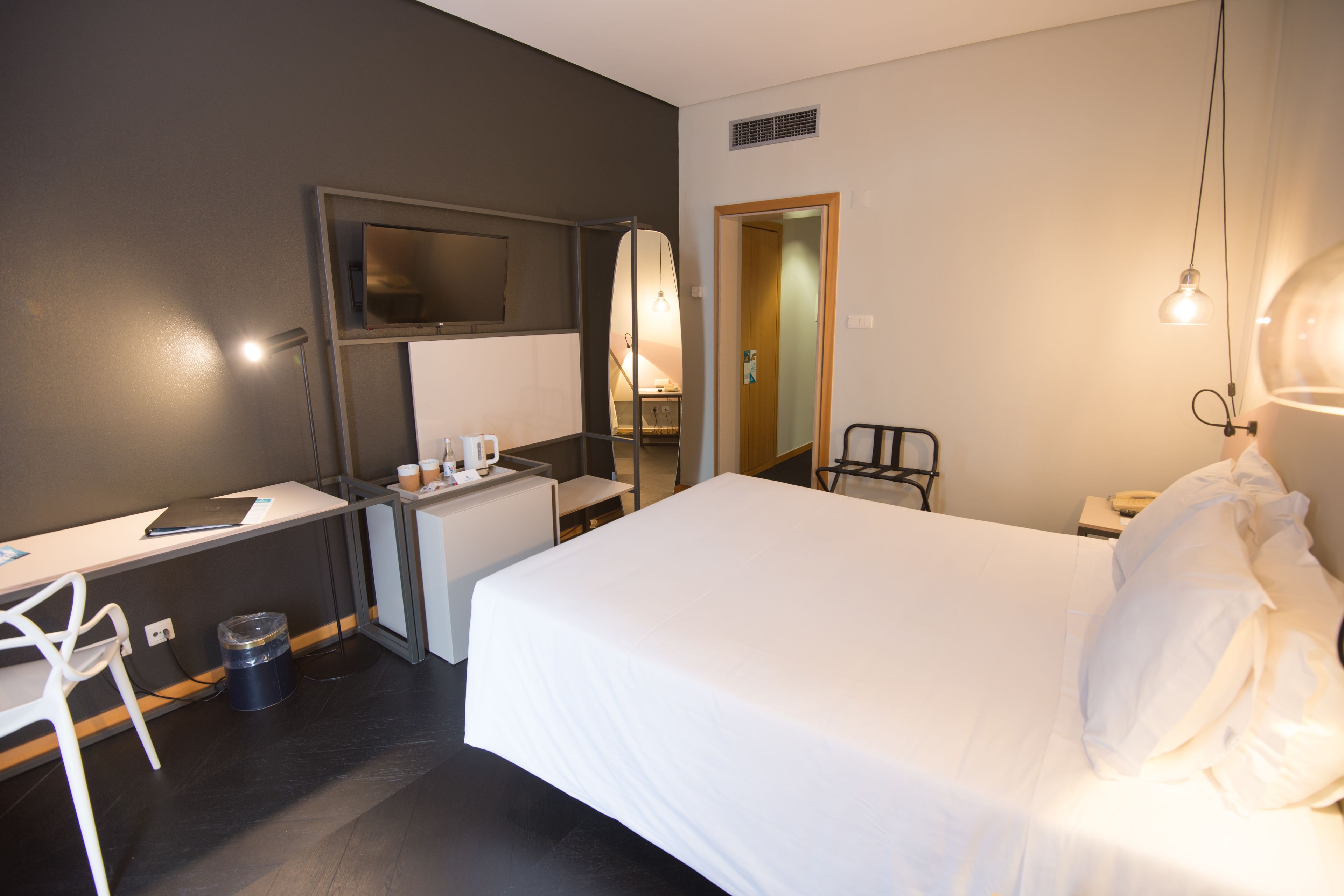 Ein Hotelzimmer mit Bett, Schreibtisch, Stuhl und einem an der Wand befestigten Fernseher.