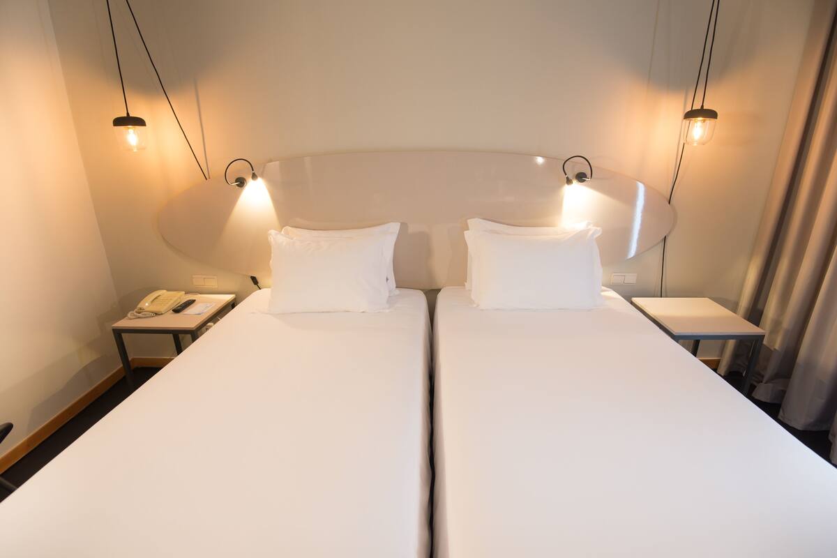 A hotel room with two single beds, a bedside table with a telephone, and a lamp on each side.