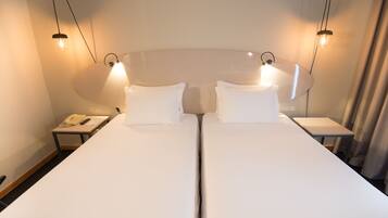 A hotel room with two single beds, a bedside table with a telephone, and two wall-mounted lamps.