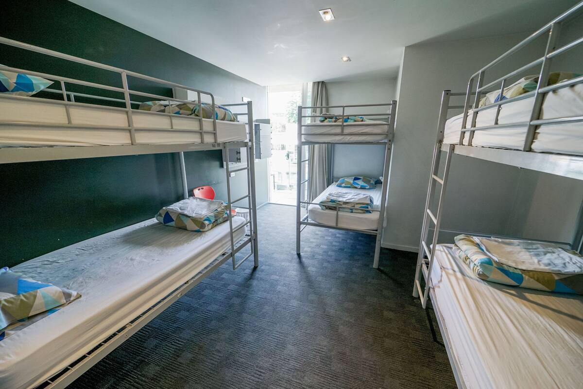 A dormitory room with bunk beds, a visible window, and a door leading outside.