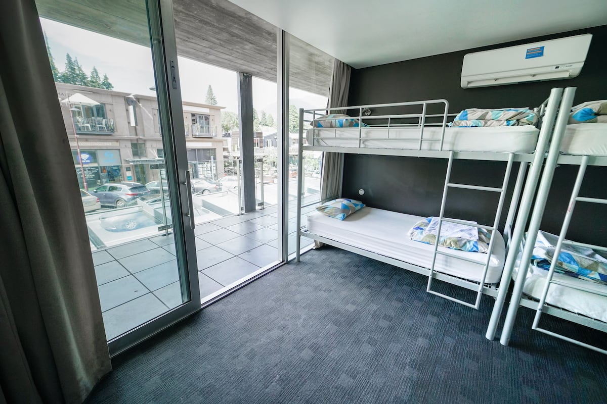 A room with bunk beds, a large window, and an air conditioning unit.