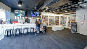 A modern office space with a reception area, bar stools, and a large screen displaying a video. - Nomads Queenstown Backpackers (Queenstown)
