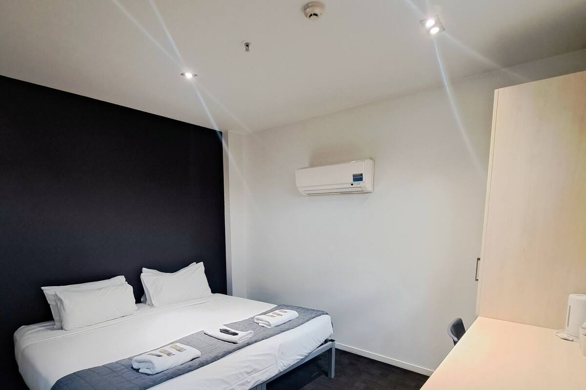A hotel room with a bed, a desk, and an air conditioning unit on the wall.