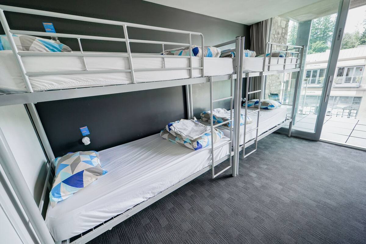 A bunk bed room with a window view, a small table, and a chair.