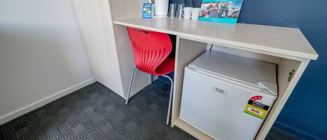 Una kitchenette compacta con refrigerador, una silla roja, cafetera y un folleto informativo sobre actividades.
