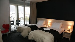 A hotel room with two beds, a red chair, and a view of the city through large windows. - Nomads Queenstown Backpackers (Queenstown)