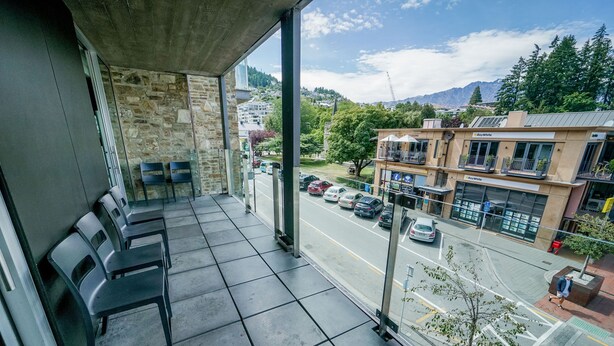 A balcony with a view of a street, stone wall, and a row of chairs. - Nomads Queenstown Backpackers (Queenstown)