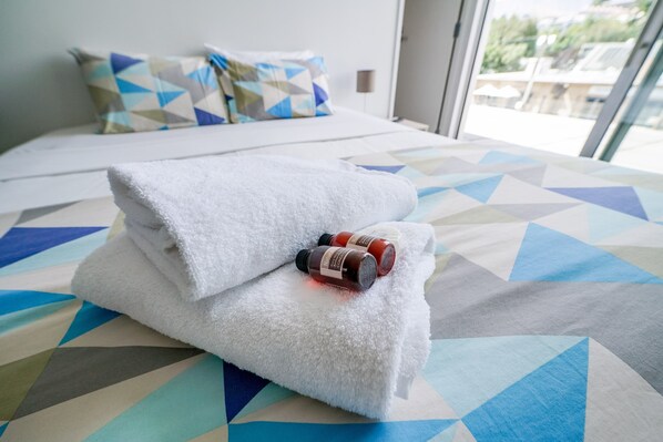 A neatly made bed with a white towel and two bottles of essential oils on top.