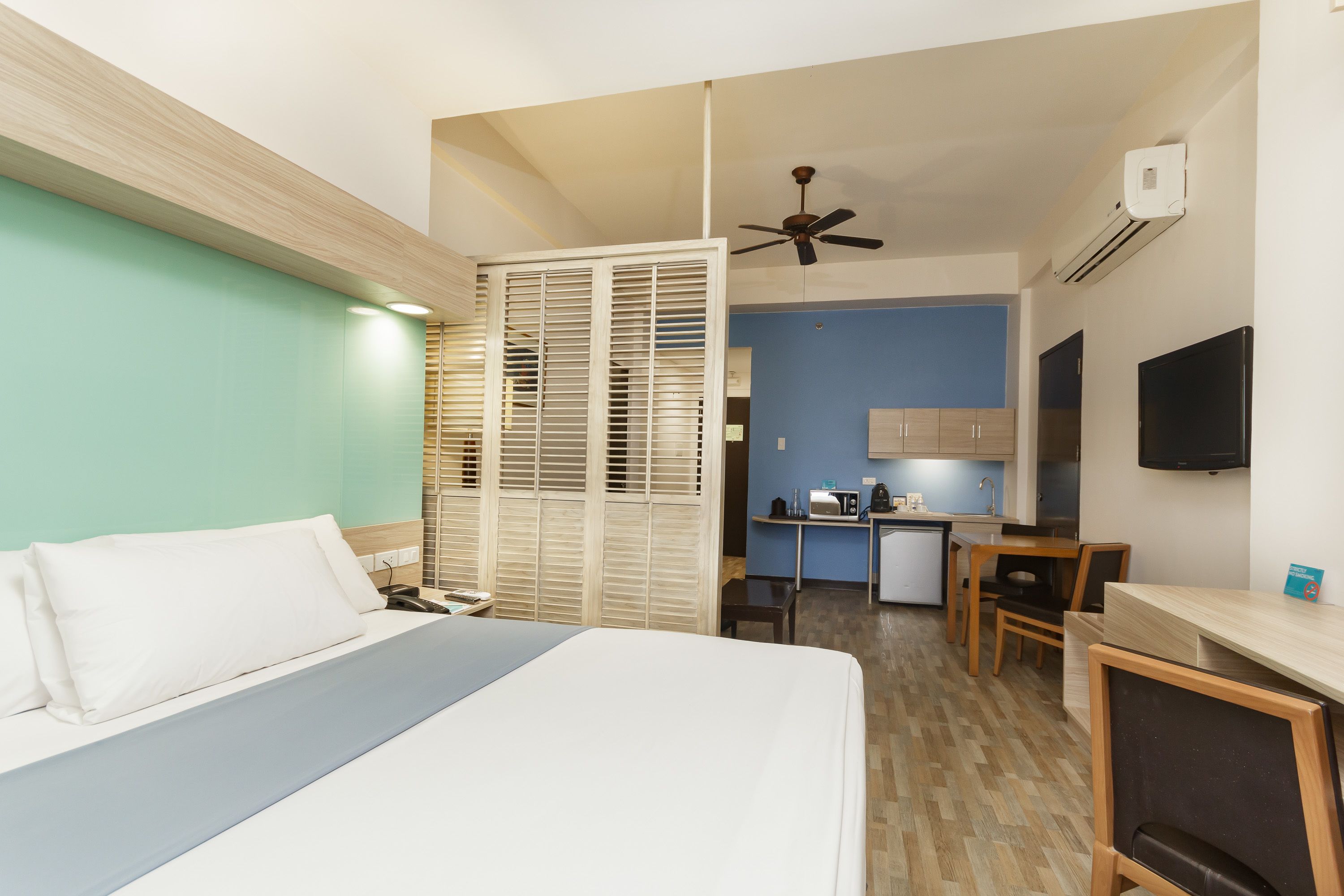 Una habitación de hotel con cama, escritorio, silla, kitchenette y televisor.