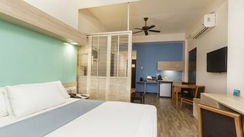 Una habitación de hotel con cama, escritorio, silla, kitchenette y televisor.