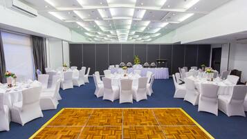 Un amplio salón de conferencias con mesas redondas, sillas blancas y un piso de madera.