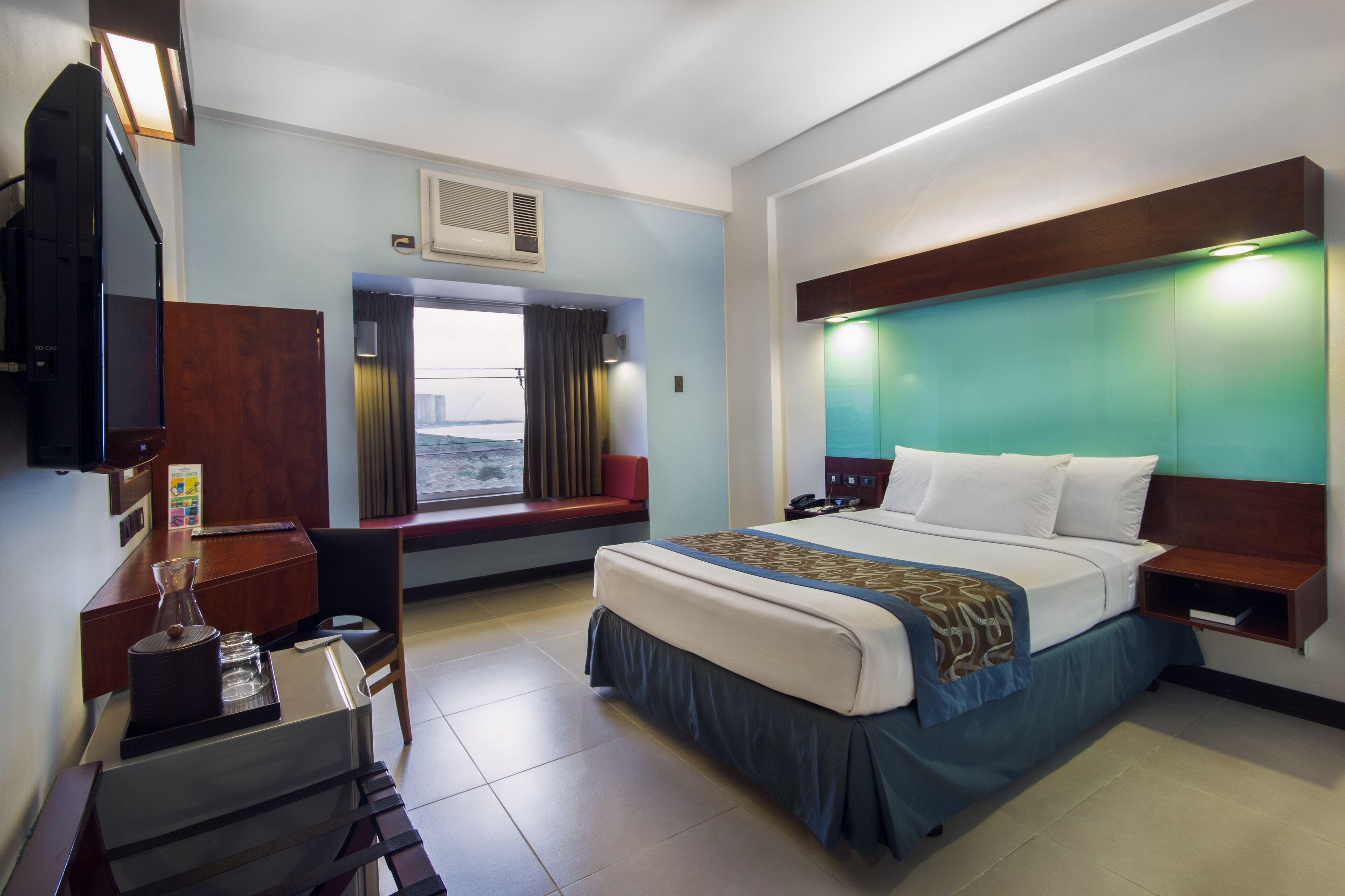 Una habitación de hotel con cama, mesita de noche, escritorio y ventana con cortinas.