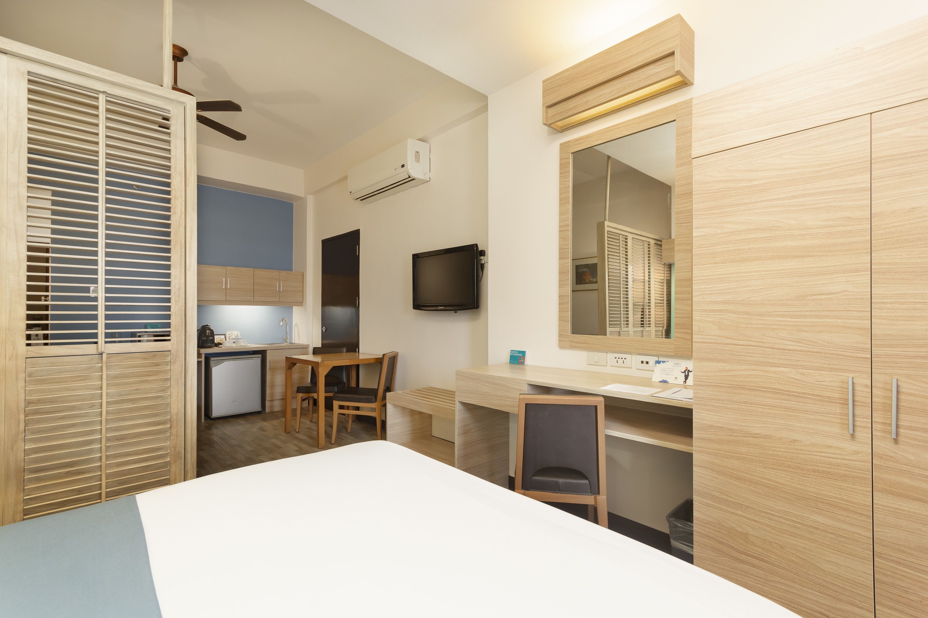 Habitación compacta con cama, escritorio, silla, kitchenette pequeño y armario.