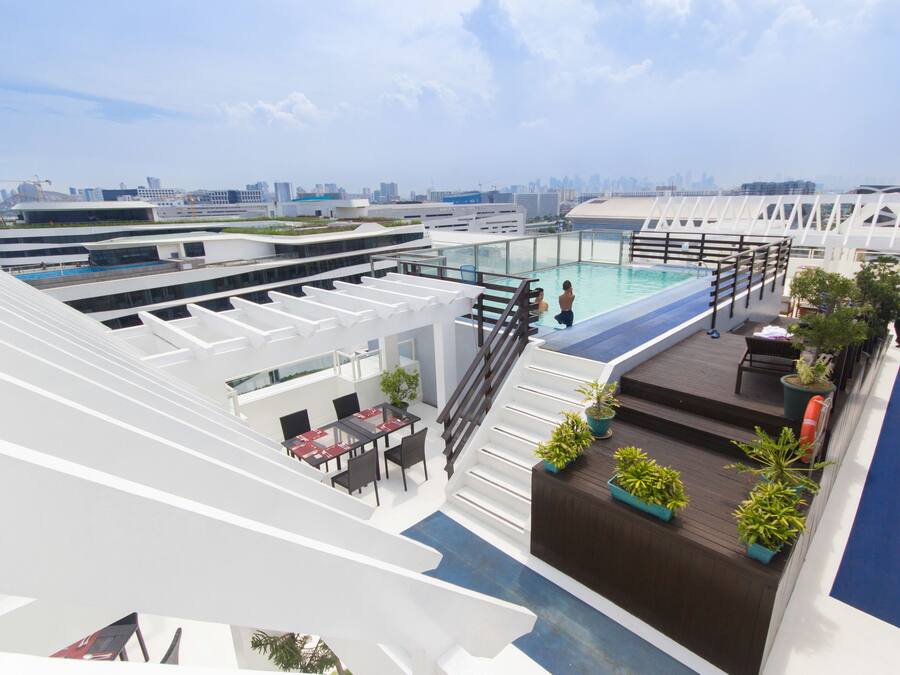 A rooftop pool area with a glass balustrade, outdoor seating, and a view of the city skyline.