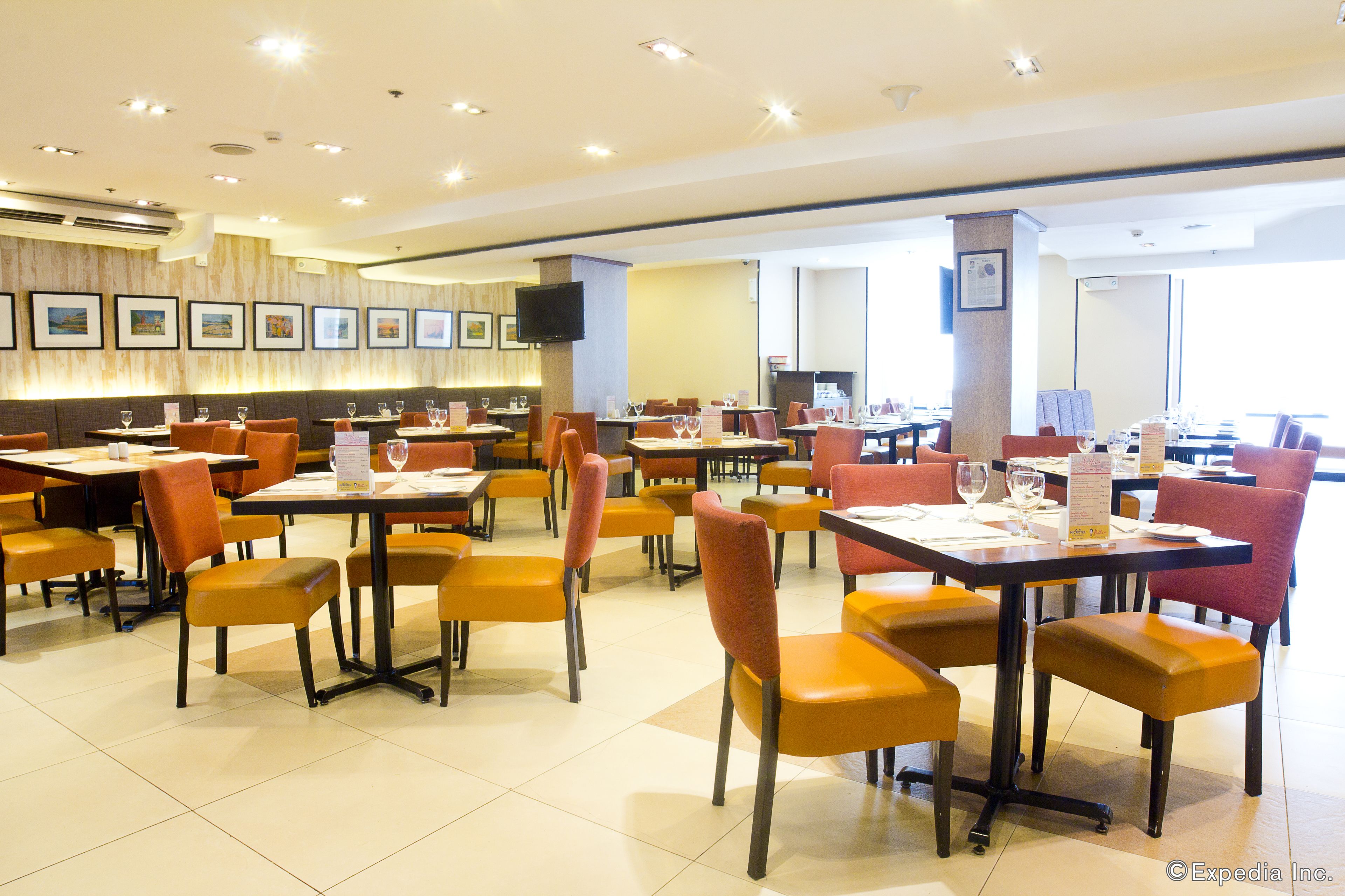 A spacious dining area with multiple tables and chairs, a flat-screen TV mounted on the wall, and framed pictures on the wall.