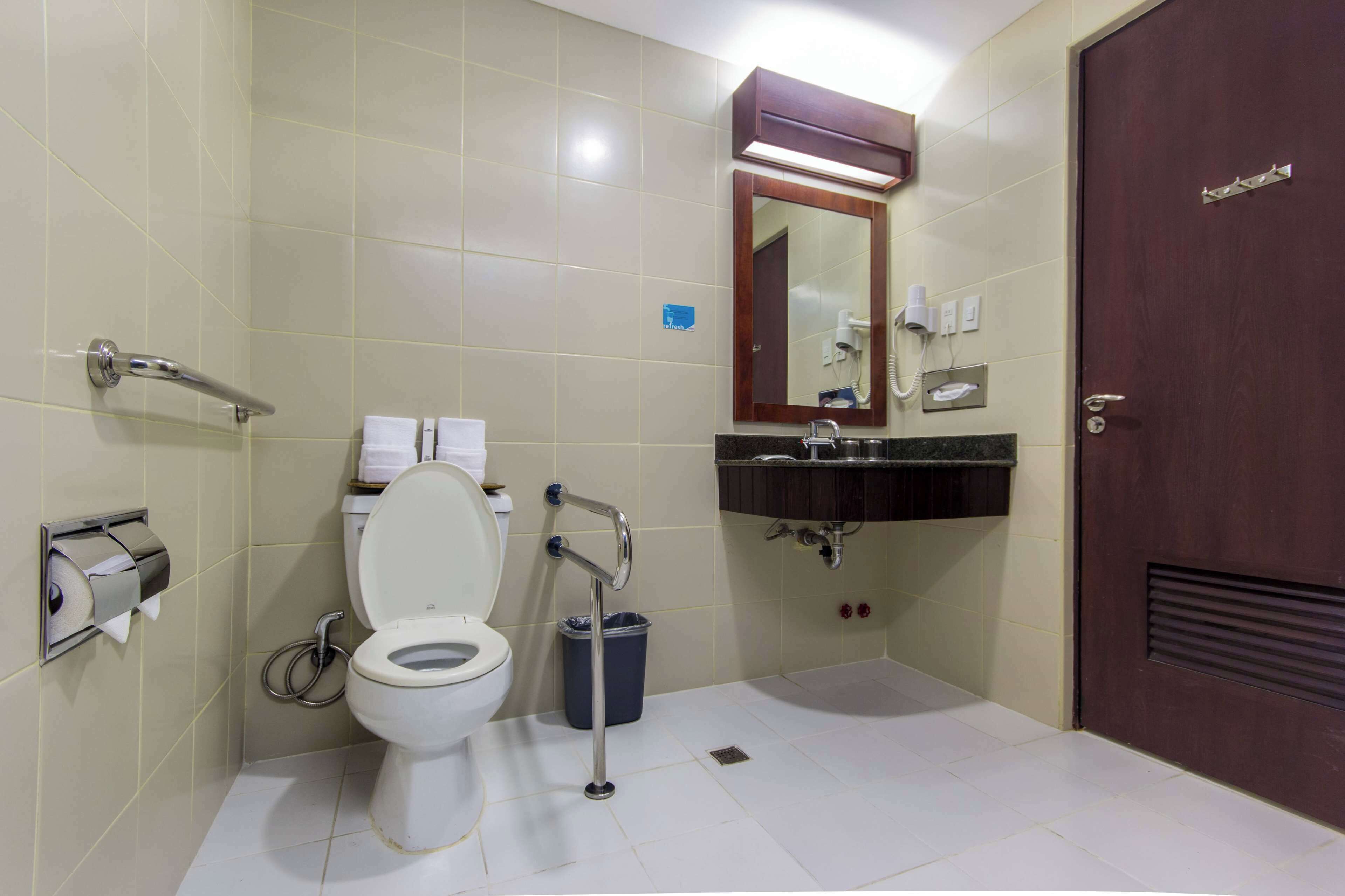 A bathroom with a toilet, hand dryer, sink, and mirror.