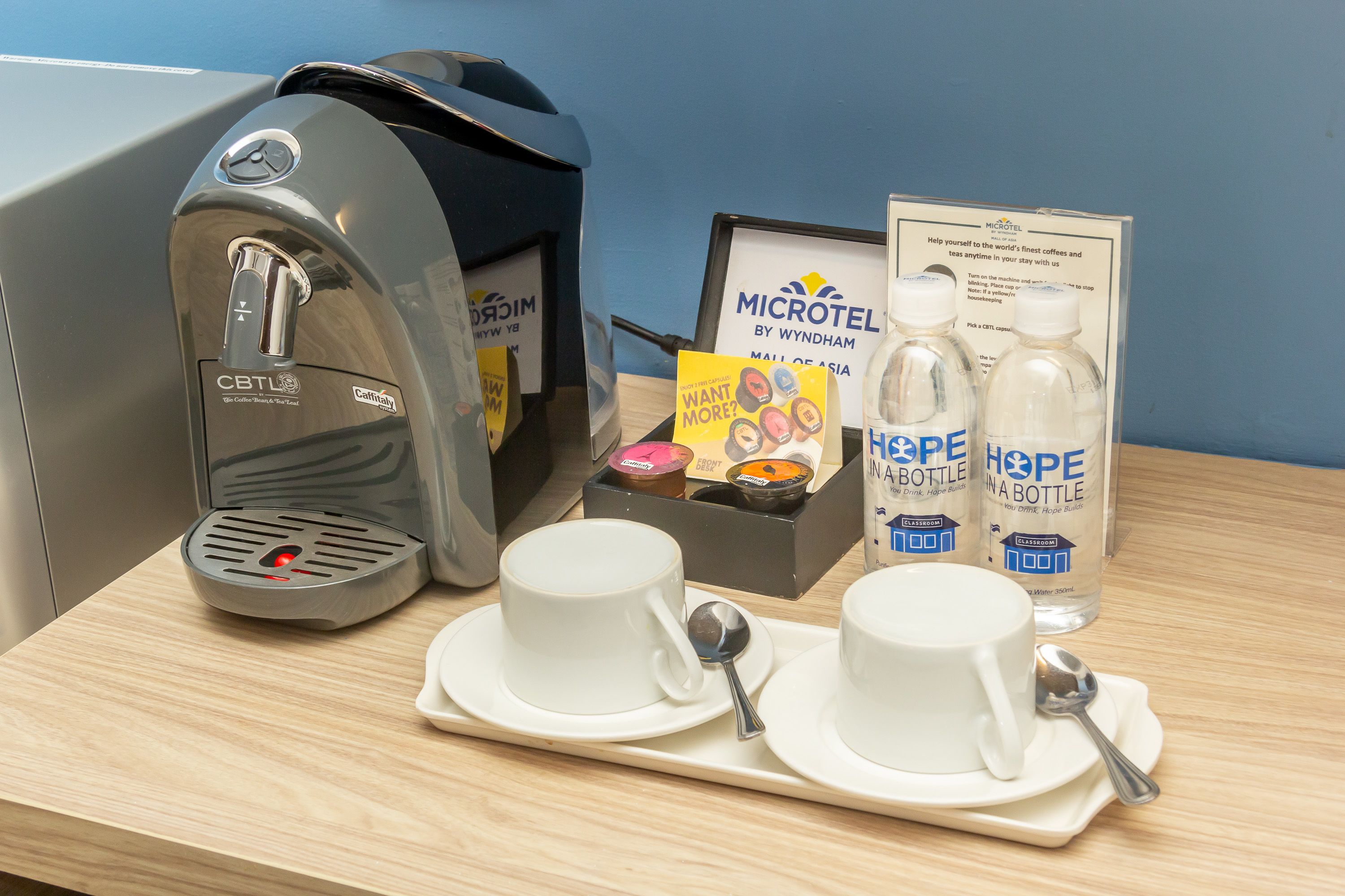 Une chambre d’hôtel équipée d’une machine à café, de deux tasses à café, d’une bouteille d’eau et d’un plateau avec une cuillère.