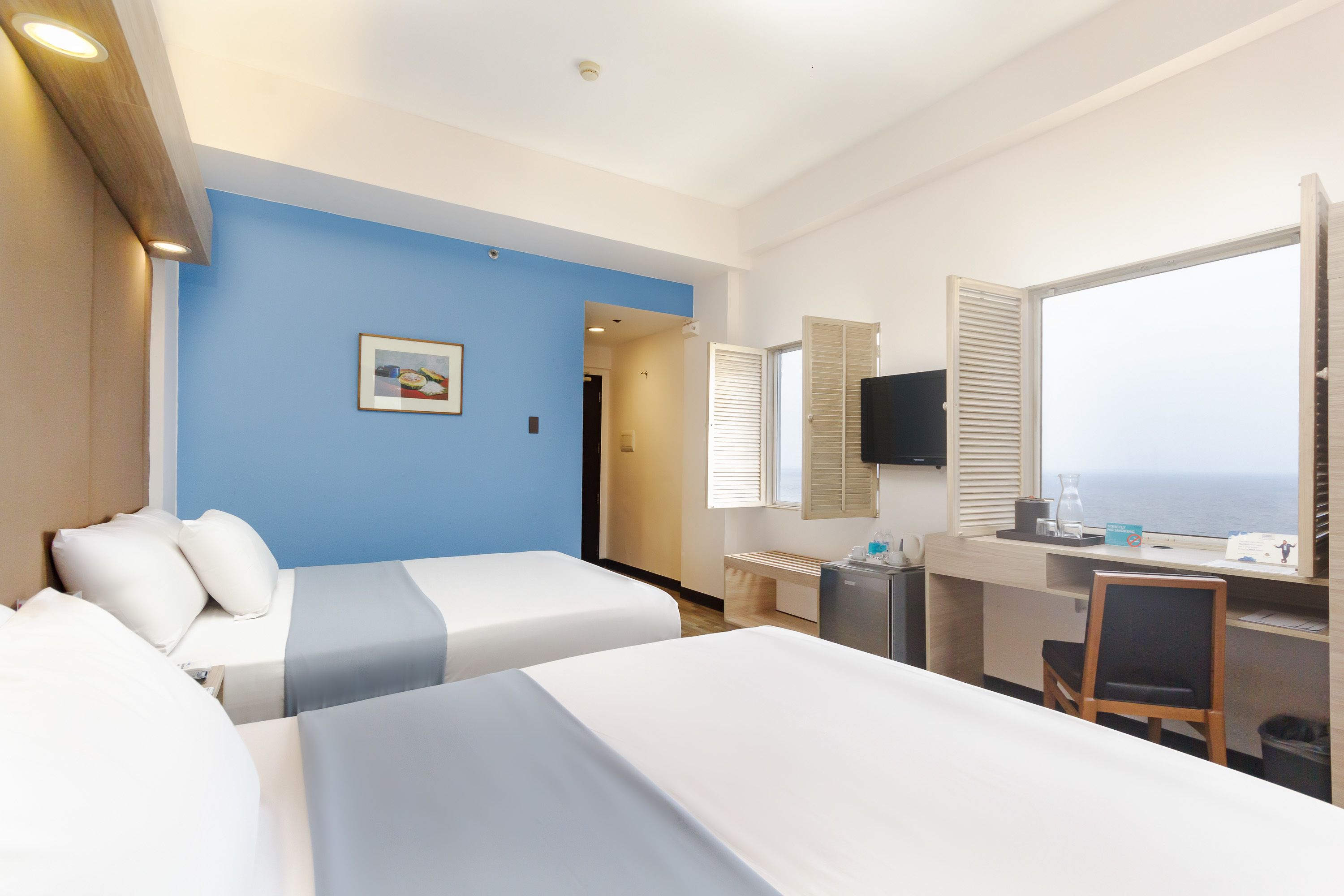 A hotel room with two beds, a desk, a chair, a TV, and a window with a view.
