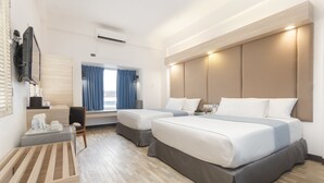 A hotel room with two beds, a desk, a TV, and a window with curtains.