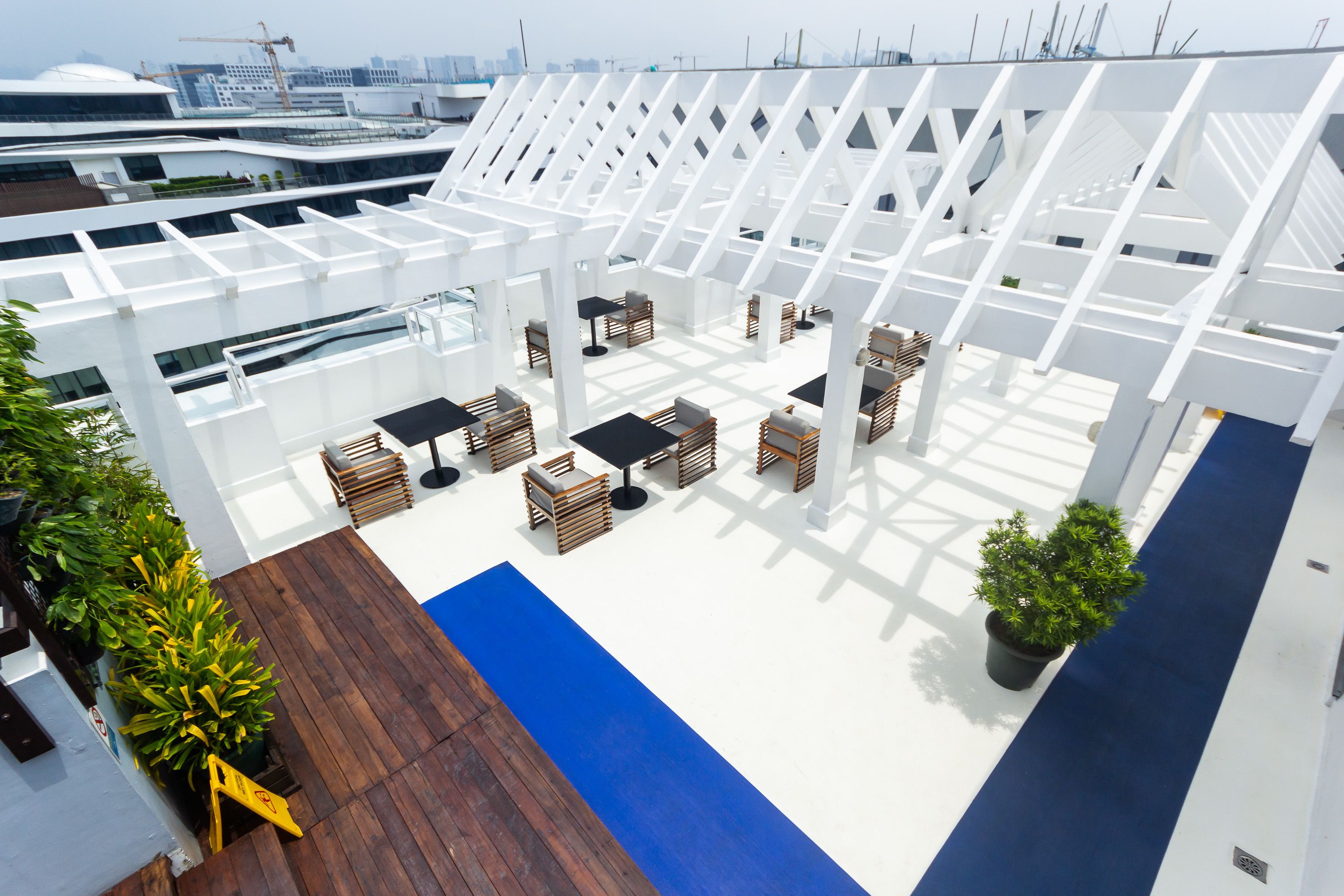 Eine Dachterrasse mit weißen Gitterstrukturen, Holzmöbeln und Topfpflanzen.
